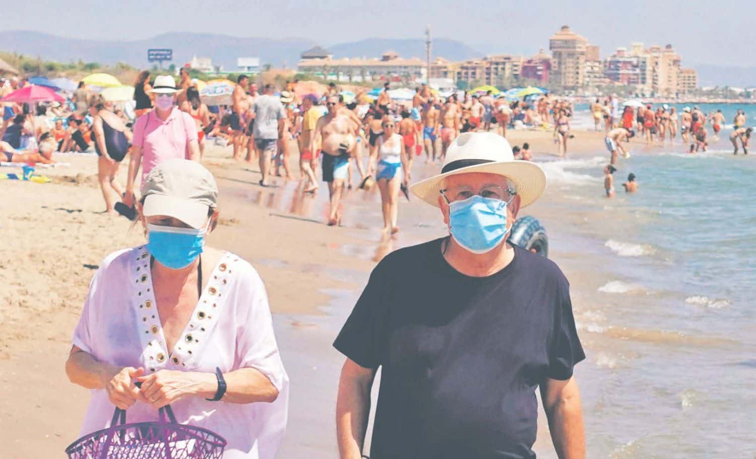 Dwoje ludzi w maseczkach spacerujący po plaży w Hiszpanii