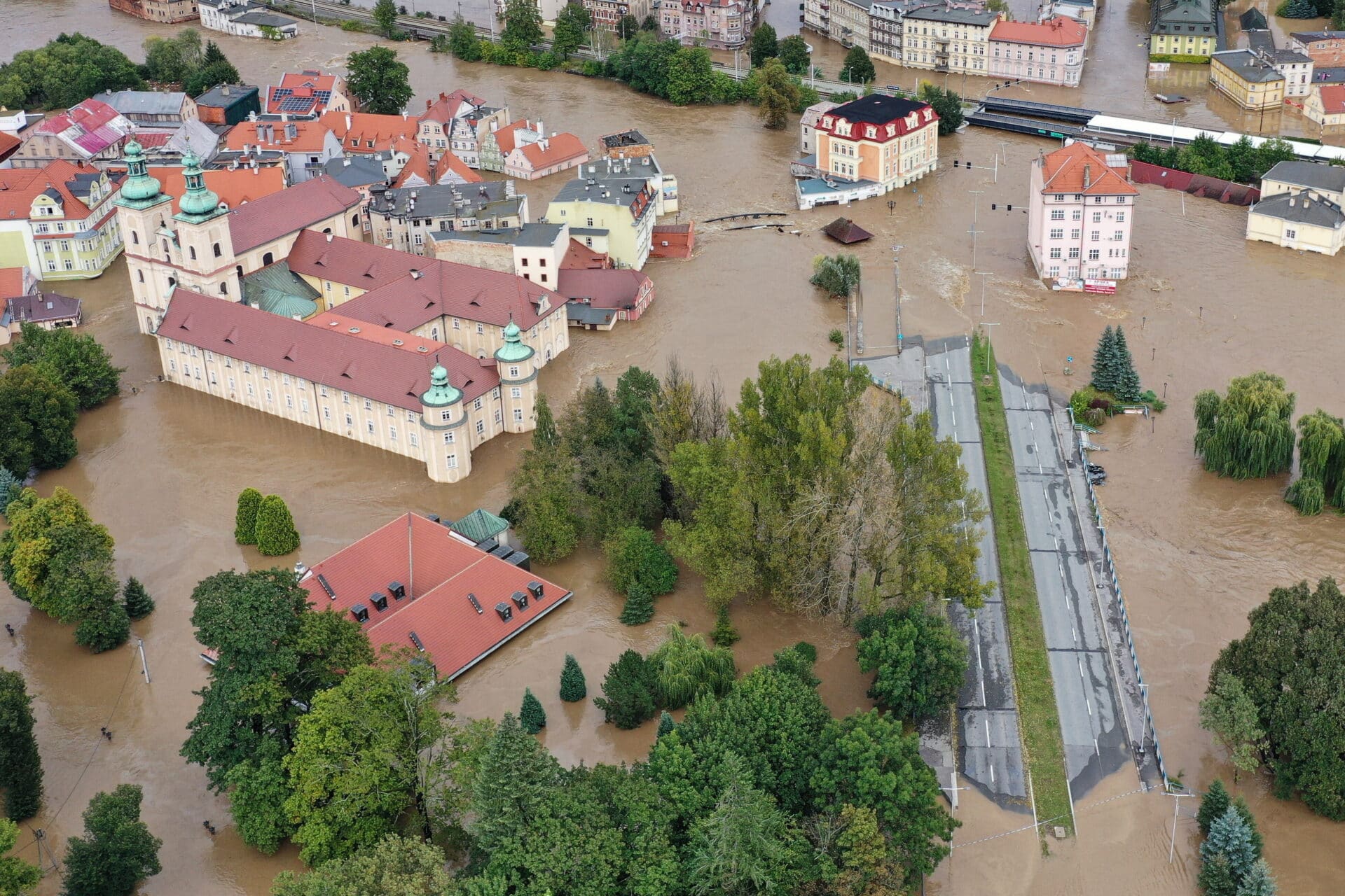 Gehenna ryb czy ludzi? Ostrzegani od lat przed zmianami klimatu w kryzysowych chwilach przekonujemy się, że największe zagrożenie stanowią niebezpieczne pomysły promowane przez zwolenników zielonej polityki. Jakub Wozinski Pamiętna powódź z 1997 r. od dłuższego czasu wydawała się co najwyżej faktem zasługującym na filmową ekranizację – odległym, mrożącym krew w żyłach, ale nie mającym już nigdy więcej prawa się powtórzyć. W chwili, gdy powstaje ten tekst, nie wiadomo jeszcze, jak wielkie szkody wyrządzi obecna powódź, ale swoim rozmachem w górnym biegu najbardziej narażonych na kataklizm rzek już teraz ściśle nawiązuje do wydarzeń sprzed niemal 30 lat. Przywracanie rzeki naturze, czyli powódź Opinia publiczna była przez lata uspokajana, że sytuacja z wielkiej powodzi nie może się powtórzyć, ponieważ przeprowadzono wielkie inwestycje w zbiorniki retencyjne, umocnienie wałów, urządzenia hydrotechniczne i systemy ostrzegania, a technologia przez trzy dekady tak bardzo się rozwinęła, że dostępne narzędzia pozwolą w porę przewidzieć zagrożenie i zapobiec tragedii. Co więc poszło nie tak? Szukając odpowiedzi na to pytanie, należałoby cofnąć się nieco do okresu wiosennego i letniego, gdy uwaga opinii publicznej (po raz kolejny od wielu lat) została zwrócona ku problemowi śniętych ryb. Wiceminister klimatu i ochrony środowiska Urszula Zielińska najpierw ostrzegała przed „gehenną ryb”, a gdy już problem się pojawił, przystąpiła ze zdwojoną siłą do przekonywania o konieczności renaturyzacji Odry. Jej zdaniem tylko przywrócenie rzece jej naturalnego biegu i przyspieszenie nurtu poprzez likwidację wszelkiego rodzaju barier mogło przyczynić się do poprawy jakości wody i rozwiązania problemów z polityką wodną. W praktyce okazało się, że prawdziwą gehennę przeżyły (i nadal przeżywają) setki tysięcy ludzi, którzy musieli się zmierzyć z wielką falą zagrażającą ich życiu oraz majątkowi. Poszkodowani będą mieli z pewnością ogromne pretensje do rządu. Premier Donald Tusk jeszcze 13 września mówił we Wrocławiu, że prognozy nie są przesadnie alarmujące i nie ma powodów do paniki, wysyłając tym samym fałszywy sygnał do powstrzymania się od działań. Gdy doszło do tragedii, Polska Agencja Prasowa usunęła swój komunikat z feralną wypowiedzią. Karygodne błędy Mieszkańcy Dolnego Śląska, Opolszczyzny czy Śląska Cieszyńskiego mogą czuć się przez władzę oszukani, ponieważ pomimo alarmujących prognoz związanych z niżem genueńskim pojawiających się już w pierwszych dniach września władze wykazały się zastanawiającą biernością. W okresie poprzedzającym nadejście wielkich opadów w Polsce panowała wielka susza, lecz zbiorniki retencyjne wciąż były mocno napełnione. Całkowicie podporządkowany klimatystycznej narracji rząd Tuska mógł mieć wręcz interes w tym, aby utrzymywać sztucznie niski stan rzek w Polsce, aby wzmocnić przekaz o rzekomo bezprecedensowych zmianach klimatycznych. Zbiorniki retencyjne w dorzeczu Odry zaczęto opróżniać dopiero w momencie, gdy powódź stała się już faktem. Zgodnie z przekazem zielonych polityków, którzy weszli w skład obecnego rządu, najlepszym sposobem zagospodarowania rzek jest renaturalizacja, tj. rezygnacja z budowy tam, zapór, regulowanych brzegów oraz przyzwolenie na istnienie naturalnych terenów zalewowych i meandrowania. To, co sprawdza się w przypadku mniejszych rzek na terenach dzikich i pojezierzach, nie ma niestety najmniejszego zastosowania w przypadku tak potężnej i niebezpiecznej rzeki jak Odra (i jej wielu dopływów). Od setek lat mieszkańcy tych ziem próbowali zaradzić okresowym powodziom, budując system tam, lecz dopiero nowoczesna technika pozwoliła przenieść tę ochronę na zupełnie nowy poziom zaawansowania i rozmachu. Pod tym względem dorzecze Odry wydaje się więc bardzo „nieekologiczne”, a jego infrastruktura przeciwpowodziowa stanowi „ingerencję w życie przyrody”. Jest to jednak absolutnie konieczne jeśli tylko chcemy zapewnić milionom ludzi bezpieczeństwo. Dążenie do renaturalizacji Odry ma jednak w Polsce zupełnie inny podtekst. Skrajnie uległy wobec Niemiec rząd Donalda Tuska niemal natychmiast po przejęciu władzy podjął się działań mających na celu likwidacji planów poprzedniej ekipy względem Odry. Zgodnie z interesem Niemiec druga największa polska rzeka miała zostać pozbawiona szeregu inwestycji mających na celu uczynienie jej bardziej żeglowną. Renaturalizacja od samego początku była niczym więcej jak tylko pretekstem do uderzenia w plany regulacji rzeki. Brak komepetencji Rzecz jasna, renaturalizacja Odry pod rządami obecnej ekipy rządzącej jeszcze nie nastąpiła, ponieważ od momentu objęcia przez nią rządów minęło raptem 9 miesięcy. Obecny rząd obciąża jednak karygodna opieszałość, zlekceważenie zagrożenia i ideologiczne zaślepienie, które nakazywało skupianie się na krzywdzie przyrody i ryb zamiast ludzi. Mający ogromny wpływ na politykę hydrologiczną w Polsce politycy, tacy jak Paulina Hennig-Kloska, Urszula Zielińska czy Mikołaj Dorożała dali się wcześniej poznać jako zieloni doktrynerzy i osoby pozbawione właściwych kompetencji potrzebnych do piastowania tak odpowiedzialnych stanowisk. Lobbowanie na rzecz zrównoważonego rozwoju i agendy klimatycznej to zupełnie inny ciężar gatunkowy niż odpowiedzialność za liczący 38 mln mieszkańców kraj i jego bezpieczeństwo. Wiele wskazuje na to, że niesłychana bierność rządzących, tak bardzo kontrastująca z zaangażowaniem ich odpowiedników w sąsiednich Czechach, wynikała głównie z braku kompetencji, ale także z chęci instrumentalnego wykorzystania zagrożenia powodziowego do nakręcenia narracji strachu przed globalnym ociepleniem. Trzeba sobie jednak powiedzieć jasno, że winę za klęskę powodzi ponoszą głównie rządzący, a nie klimat, ponieważ obfite deszcze pojawiają się w tym regionie cyklicznie od wielu stuleci. Obecnie mamy zaś do czynienia z próbą zrzucenia odpowiedzialności za popełnione błędy, o czym świadczy choćby wydany przez prezydenta Wrocławia Jacka Sutryka komunikat mówiący o „błędnych prognozach hydrologów”. Gdyby błędne były tylko prognozy specjalistów, to czy z mediów publicznych i społecznościowych usuwano by wcześniejsze wypowiedzi premiera i ministrów? Zielony lobbing jest dziś niezwykle łatwym i dobrze płatnym zajęciem, dlatego przyciąga osoby niekompetentne. W sytuacji, gdy narrację klimatyczną uskuteczniają wielkie media, korporacje, organizacje międzynarodowe i rządy, osoby zaangażowane w zielony trzeci sektor nie muszą się nawet szczególnie wysilać, ponieważ ciężar argumentacji biorą na siebie inni. Problem pojawia się jednak w momencie, gdy zieloni lobbyści obejmują odpowiedzialne stanowiska i jako członkowie rządu decydują o bezpieczeństwie milionów osób. Obecna powódź, która doprowadziła do tak wielkiej liczby osobistych tragedii, powinna zadziałać jako ważny sygnał ostrzegawczy, aby więcej nie ulegać presji zielonych doktrynerów. Los ludzi jest zdecydowanie ważniejszy niż los ryb, a ekologia musi być podporządkowana dobru ludzkiemu. Prace na Odrze, które zgodnie z oprotestowywaną od lat specustawą poprzedniego rządu zakładały budowę kolejnych zbiorników retencyjnych i regulacje rzeki, muszą zostać bezwarunkowo wznowione. W centrum uwagi musi się przy tym znaleźć ponownie człowiek oraz jego potrzeby. I oczywiście potrzeby polskiego, a nie niemieckiego państwa.